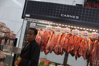A client stands next to pieces of meat for sale at a butcher shop in Rio de Janeiro