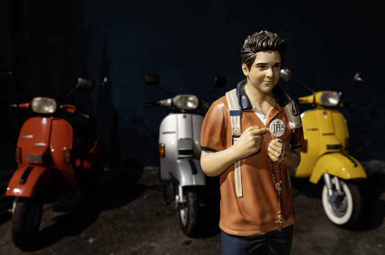 Escultura de Carlo Acutis com mochila nos ombros a frente de motos Vespas na exposição sobre o próprio Carlo Acutis, "o santo de calça jeans" que será canonizado no Vaticano no próximo domingo dia 07.