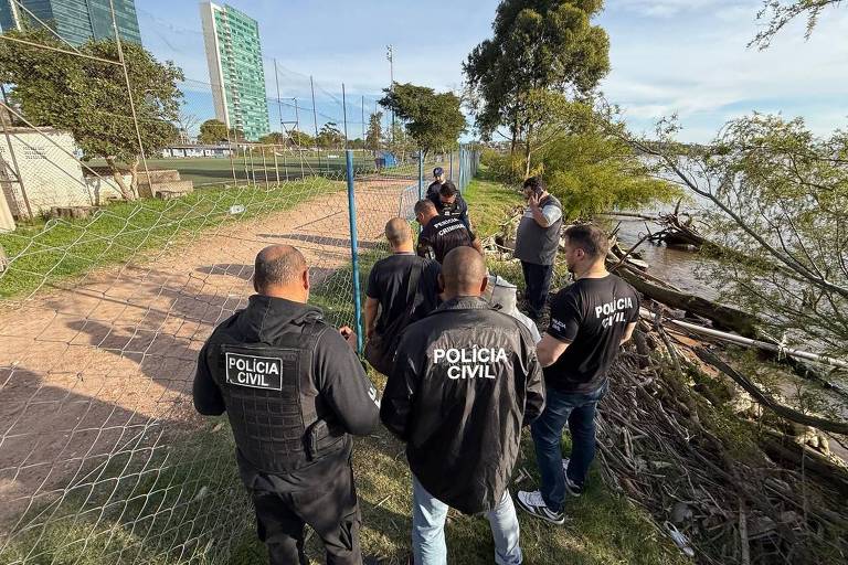Группа сотрудников гражданской полиции собралась на открытой площадке у водоёма. Они одеты в чёрные жилеты с надписью «ГРАЖДАНСКАЯ ПОЛИЦИЯ». На заднем плане видны забор, деревья и высокие здания. Судя по всему, идёт какая-то операция или расследование.