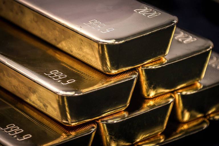 Seis barras de ouro empilhadas em duas camadas sobre superfície refletiva preta. Cada barra tem a marcação '999.9' indicando pureza e um número de série gravado na superfície.