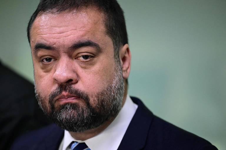 Homem de meia-idade com barba e cabelo curtos, vestindo terno escuro, camisa branca e gravata, com expressão séria e olhar direto.