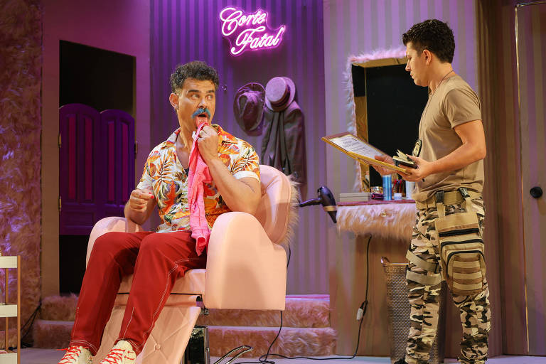 Dois homens em um salão de barbearia. Um está sentado em uma cadeira rosa, vestindo camisa florida e calça vermelha, segurando um pano rosa na boca. O outro está em pé, vestindo camiseta bege e calça camuflada, segurando uma prancheta. Ao fundo, parede com chapéus pendurados e letreiro neon rosa escrito 'Corte Fatal'.