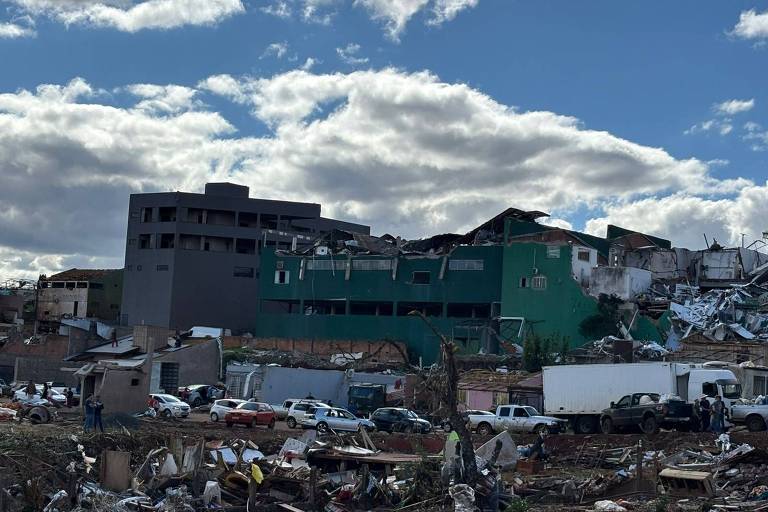 Kentsel bir alana dağılmış enkazlarla kısmen yıkılmış binalar. Bulutlu gökyüzünün altında ön planda park etmiş araçlar ve enkaz görülüyor.