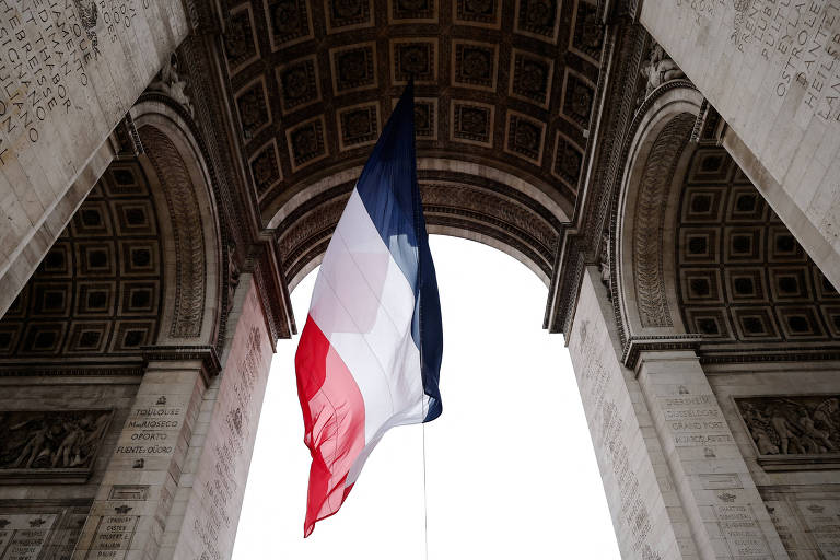 Bandeira tricolor da França pendurada sob o Arco do Triunfo em Paris, vista de baixo para cima, com detalhes arquitetônicos do arco visíveis nas laterais e no teto.