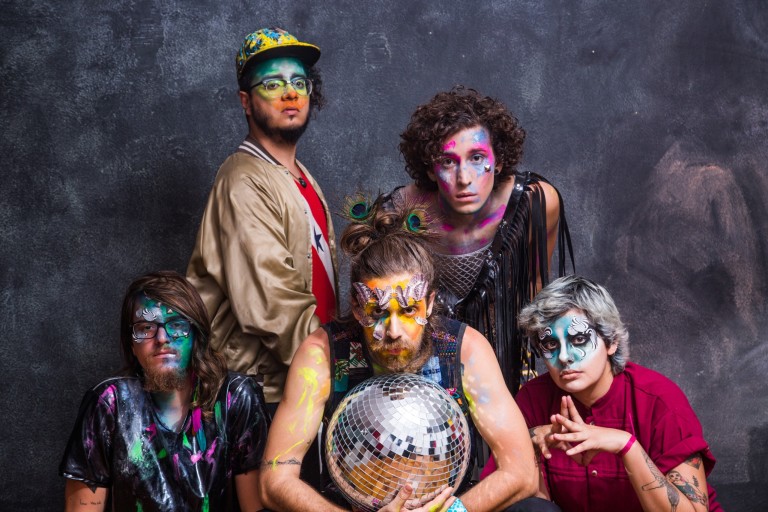 Os cinco integrantes da banda posam para foto com os rostos pintados com tintas coloridas